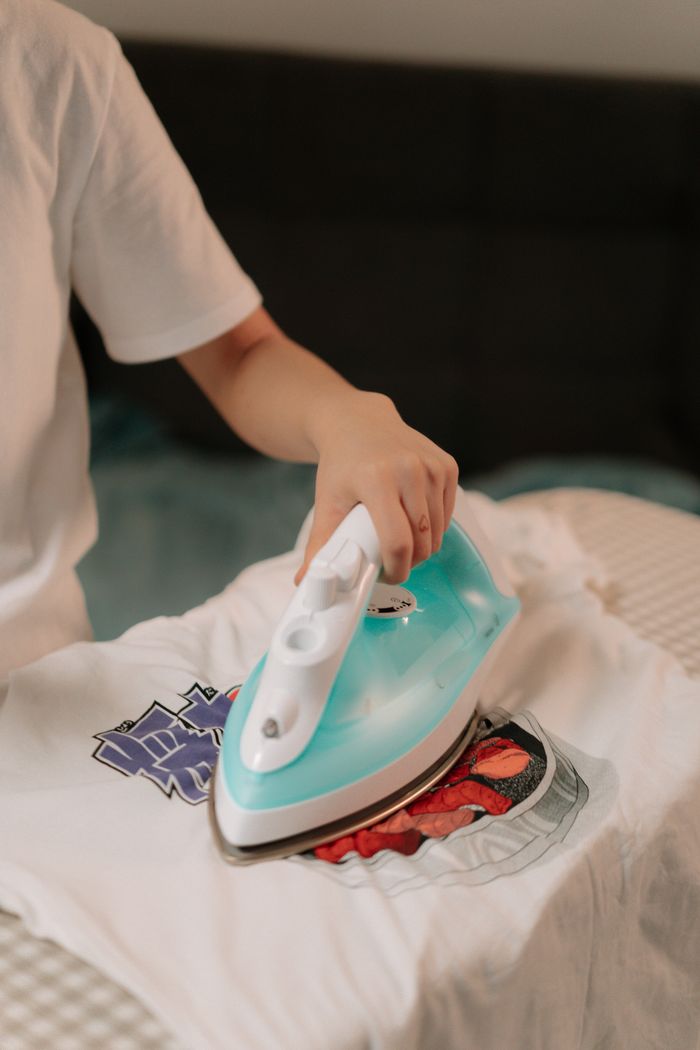 why-choose-us-01 Close-up of a person ironing a graphic t-shirt on an ironing board at home.