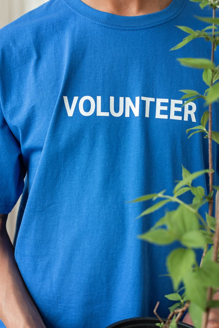 why-choose-us-02 Blue-shirted volunteer with plant, reflecting community work and environmental care.